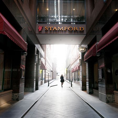 스탬포드 플라자 멜버른 호텔 멜번 외부 사진 The photo depicts a narrow alley or passageway, possibly in an urban setting. On one side, there are storefronts with canopies, and on the opposite side, there is a prominent sign reading "STAMFORD." The pathway is lined with buildings, creating a se