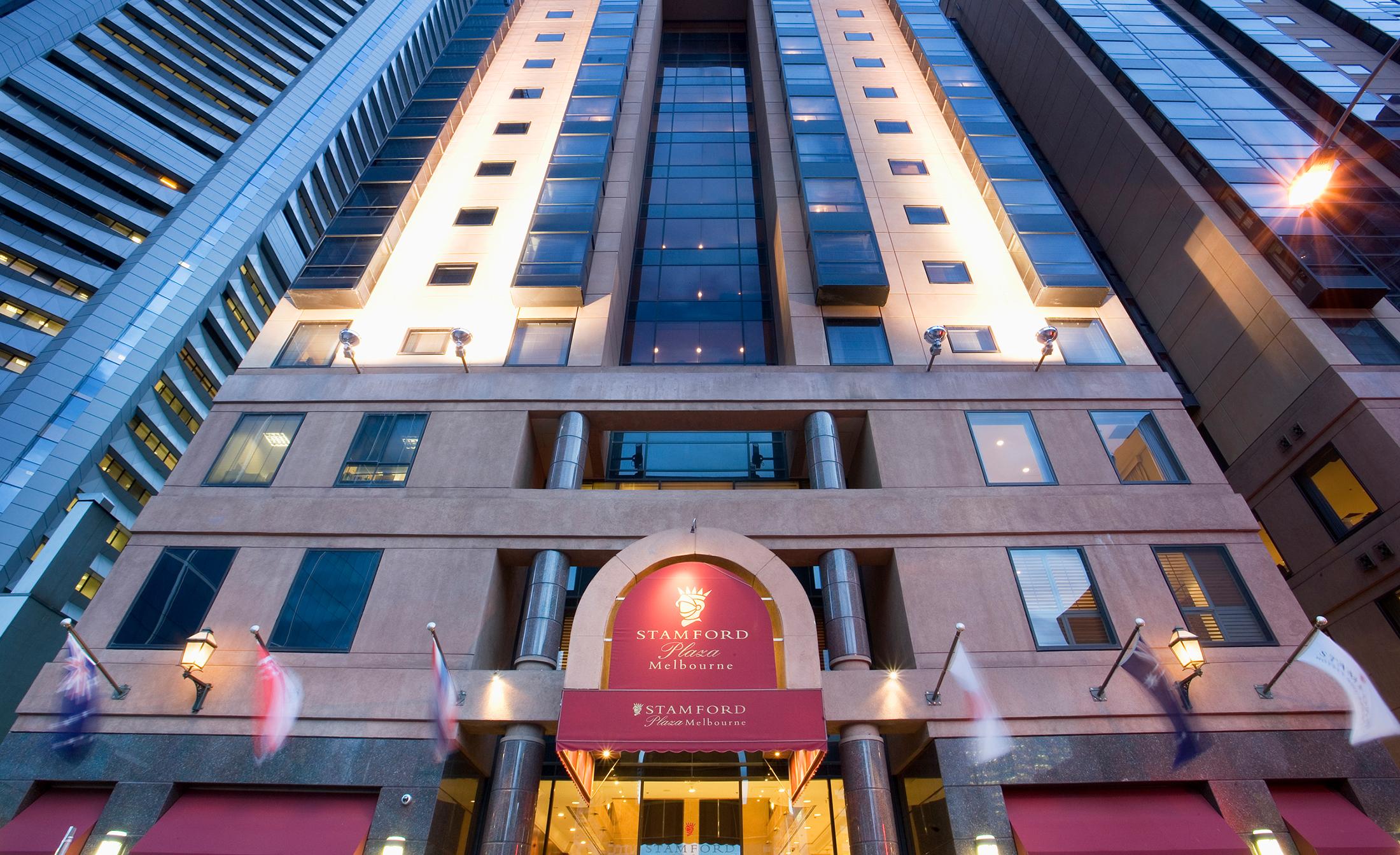 스탬포드 플라자 멜버른 호텔 멜번 외부 사진 The photo shows the entrance of a modern hotel building. The architecture features a tall structure with glass and stone elements. The hotel's name is visible above the entrance, which is framed by an arch, and the facade includes multiple levels wit