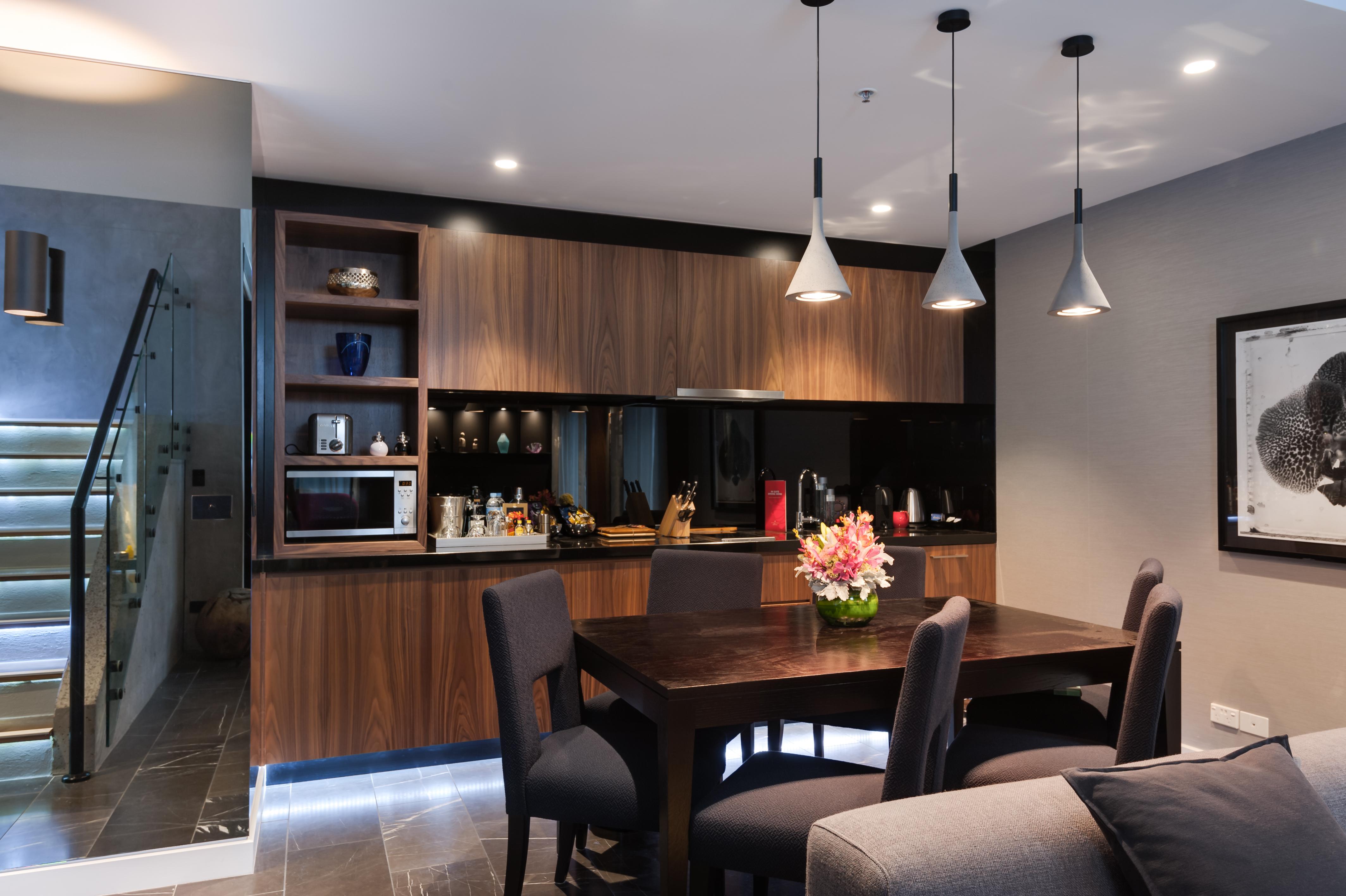 스탬포드 플라자 멜버른 호텔 멜번 외부 사진 The image shows a modern kitchen and dining area. The kitchen features dark wooden cabinetry with black accents, a microwave, and various kitchen items arranged on the shelves. There is a dining table made of dark wood, surrounded by several chairs. 