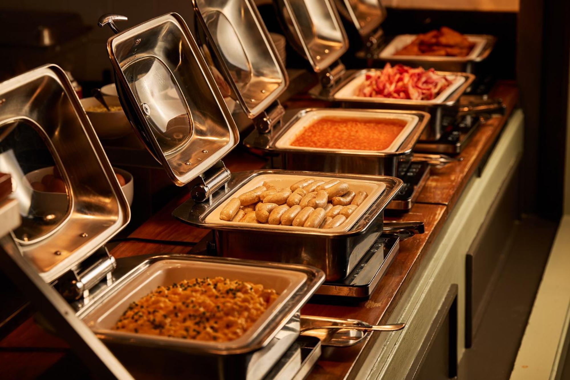 스탬포드 플라자 멜버른 호텔 멜번 외부 사진 The photo depicts a buffet setup featuring multiple food trays in stainless steel chafing dishes. Each dish is opened to display different types of food. The dishes contain a variety of items, which might include a mix of proteins, vegetables, or sta
