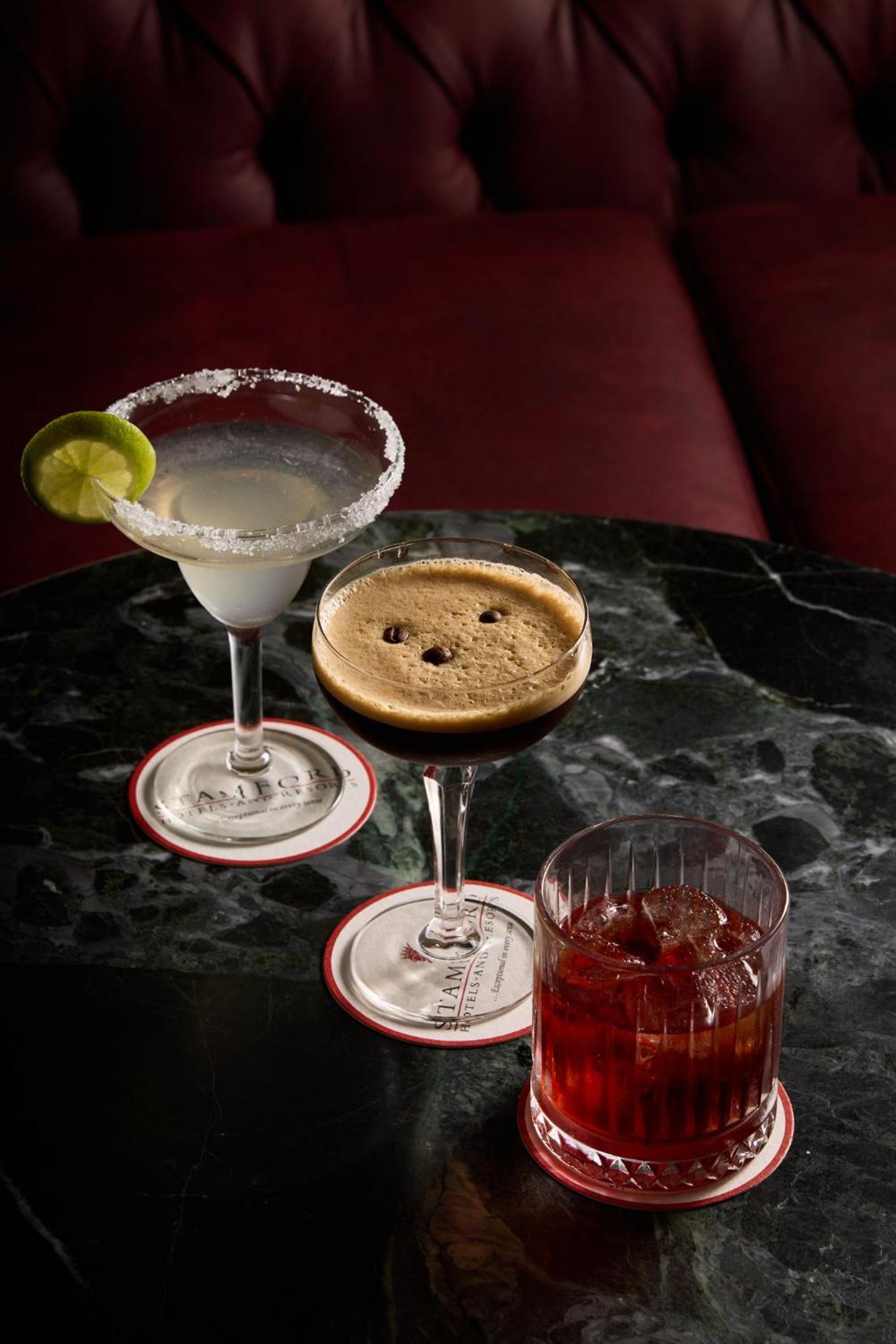 스탬포드 플라자 멜버른 호텔 멜번 외부 사진 The photo displays three different cocktails arranged on a dark marble table. 

1. On the left, there is a margarita glass filled with a clear drink, garnished with a lime slice and featuring a salted rim.
2. In the center, a coupe glass holds a dark