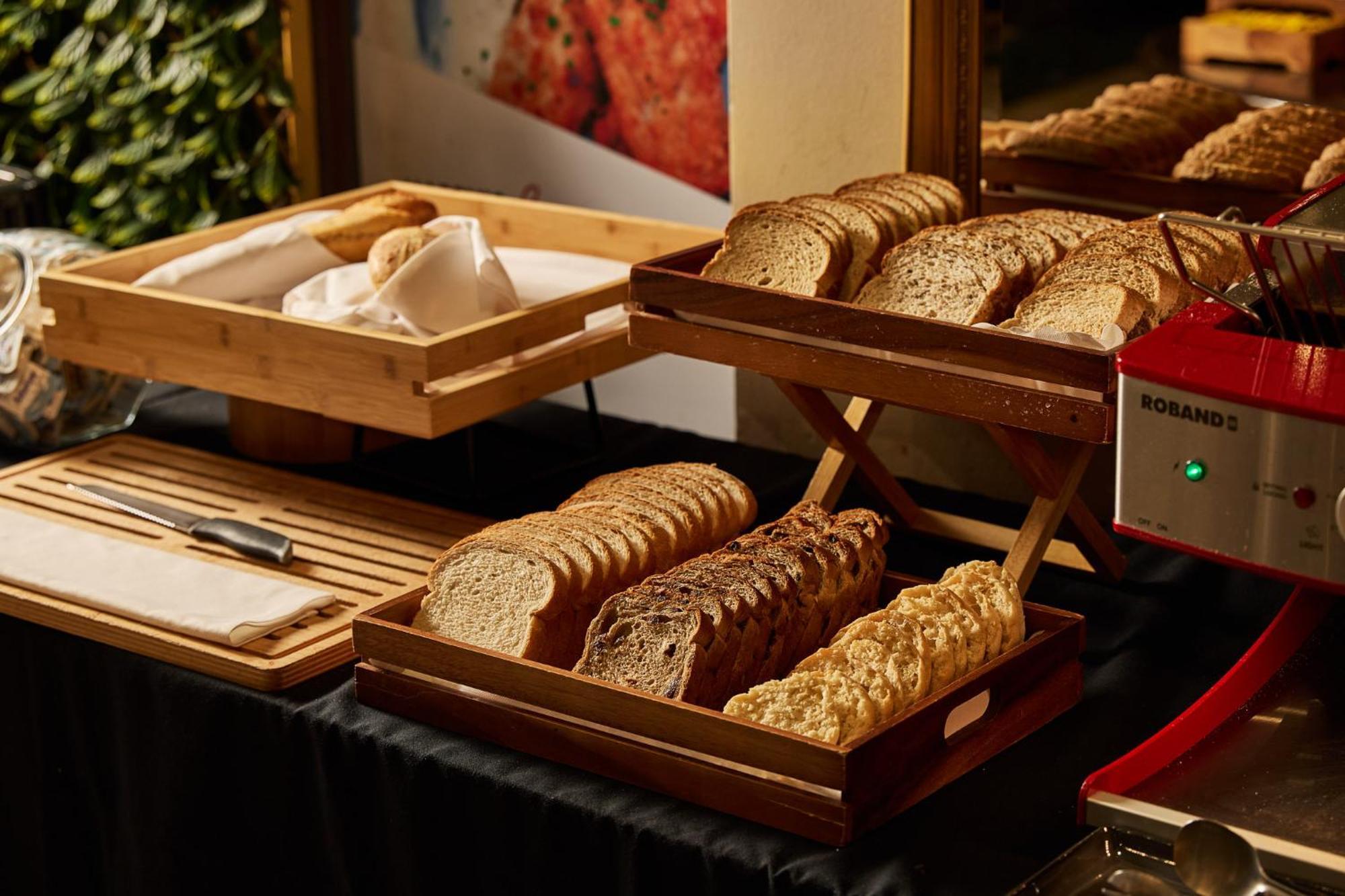 스탬포드 플라자 멜버른 호텔 멜번 외부 사진 The photo shows a display of various types of bread arranged on wooden trays. There are several stacks of sliced bread, including light and dark varieties. One tray appears to hold a selection of whole grain or multigrain bread, while another feature