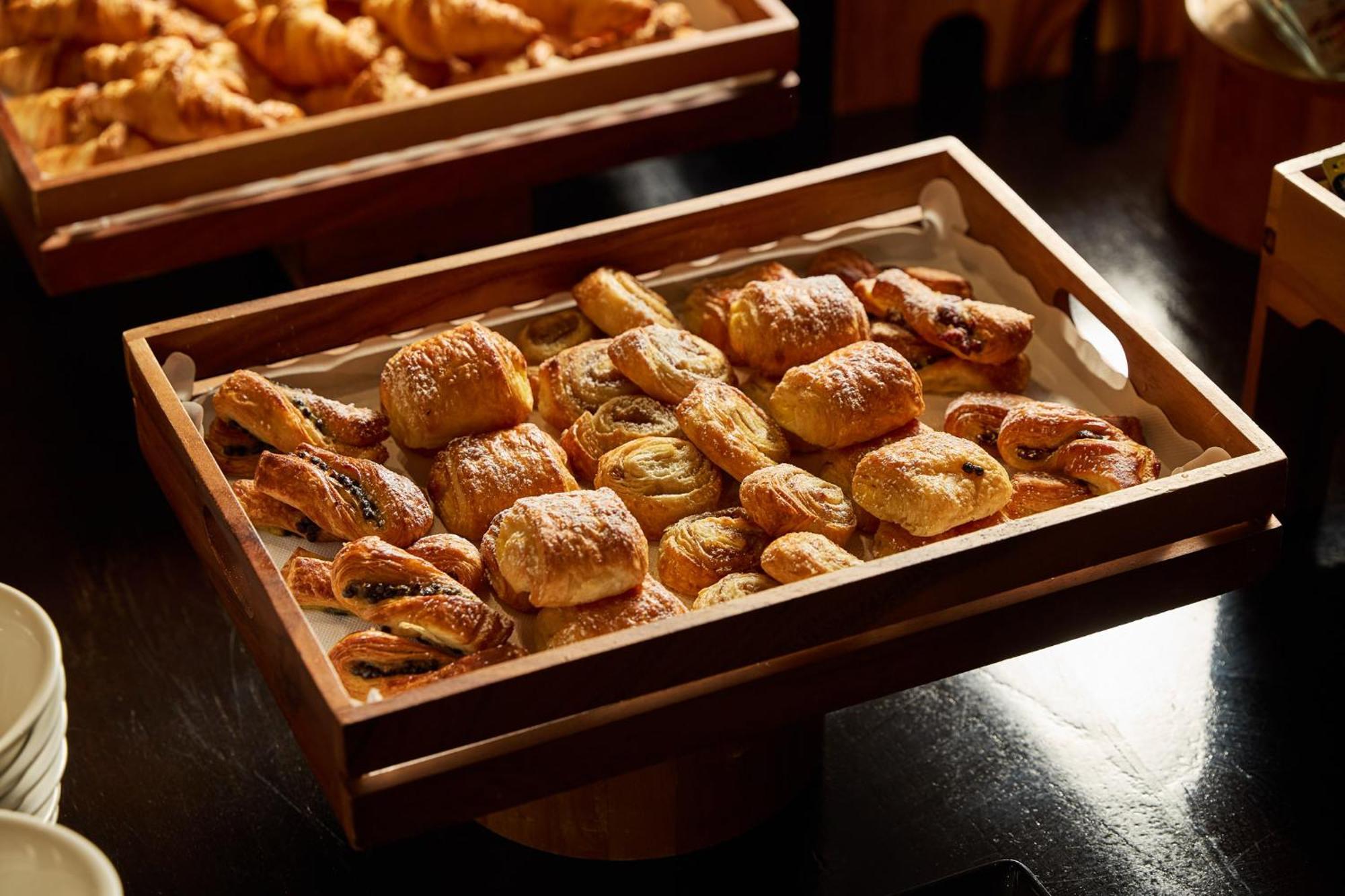 스탬포드 플라자 멜버른 호텔 멜번 외부 사진 The photo shows a wooden tray filled with an assortment of baked goods. There are various types of pastries, including small, flaky items that appear to be puff pastries, and possibly some filled with chocolate or fruit. The pastries are golden brown