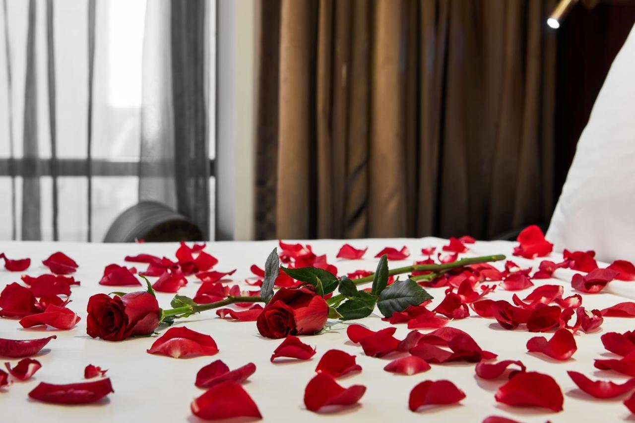 스탬포드 플라자 멜버른 호텔 멜번 외부 사진 The photo shows a bed or a table covered with scattered red rose petals. Among the petals, there are a few whole red roses, still with their stems. The background features curtains that appear to be sheer, allowing some light to come through, and the